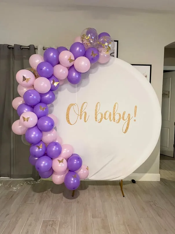 Purple and pink half-arch balloon garland with gold butterflies on a round Oh Baby backdrop by CAJE Creations, Tampa FL
