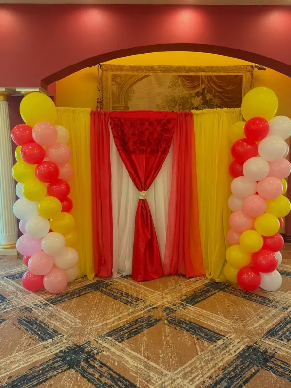 Red and gold drape backdrop framed by red, pink, yellow and white balloon columns by CAJE Creations, Tampa Bay